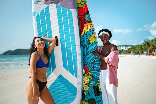 Young multiethnic people, couple having fun on surfboards in the clear ocean water during summer