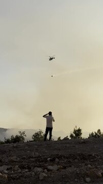 Distant view of concerned people witnessing a destructive woodland fire and aerial response