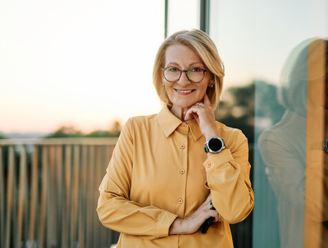 Portrait of a middle aged mature businesswoman woman using a smartphone mobile phone walking down the street, surrounded by moderncorporate office buildings
