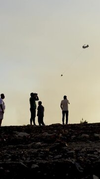 Worried residents standing on a hill observing heavy dark smoke and firefighting helicopters
