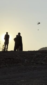 Anxious locals watching a massive pine forest wildfire from a distance at sunset