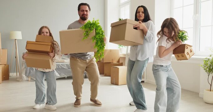 Family parents dancing children moving boxes. They dance while carrying plants and cartons in a bright living room, celebrating relocation and a fresh start. Happy family moving day concept.