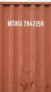 Close-up of a rusty shipping container with white alphanumeric code and weathered surface