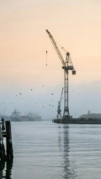 Construction Crane on Waterway at Sunset with Ships and Birds in the Background