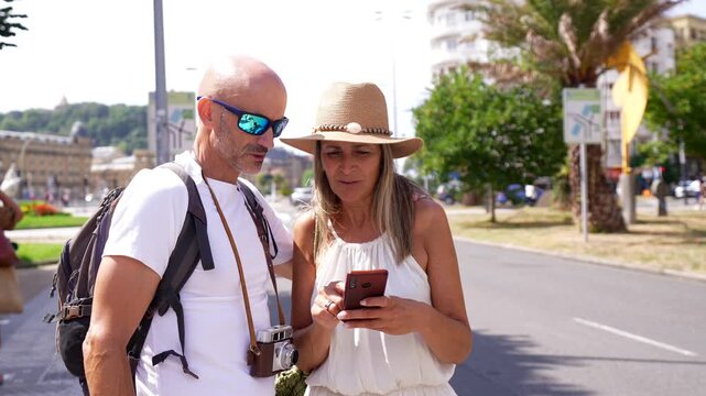 Happy senior couple exploring a new city on a sunny day, using a mobile phone with a map application to find their way, enjoying their summer vacation and retirement together