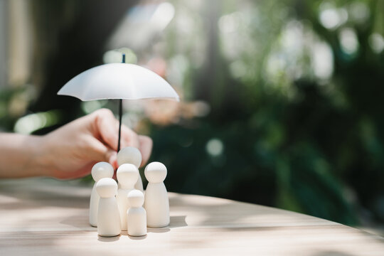 Family protection concept. Umbrella sheltering wooden family figures represents life insurance and household security, safety, care, support, stability