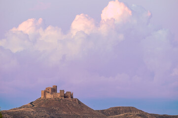 Obraz premium Medieval Castle of Montearagon perched on top of a hill under dramatic purple sunset storm clouds, iconic romanesque fortress silhouette near Huesca, Aragon, Spain.