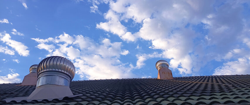 Stainless steel roof ventilator spin on tile roof with blue sky. Roof exhaust ventilation fan ball on factory or house roof, Air ventilator mechanism installed. not ai