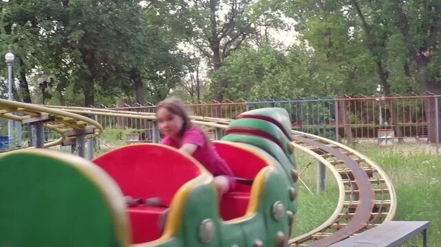 Young girl having fun while riding a colorful caterpillar shaped kiddie roller coaster in a park