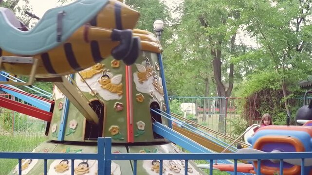 Little girl riding a vintage flying bee carousel attraction in an old amusement park