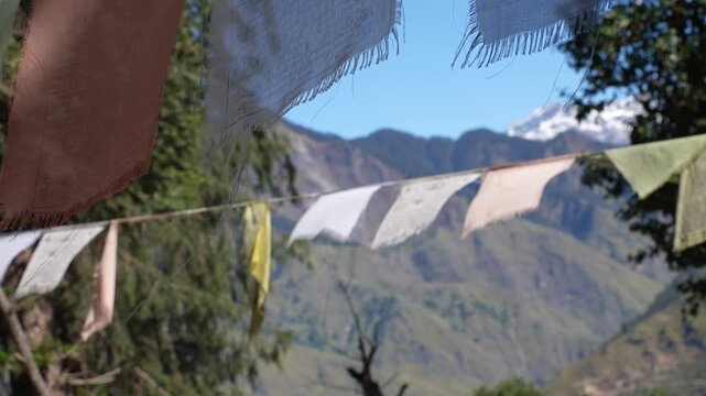 Close-up cinematic view of colorful Buddhist prayer flags fluttering in the mountain wind, with majestic Himalayan peaks softly blurred in the background. The shallow depth of field highlights the spi