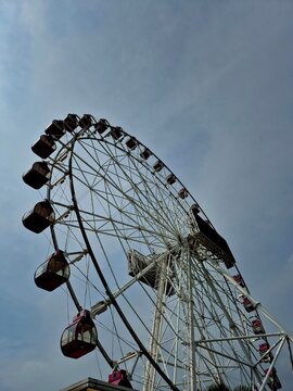 a giant Ferris wheel from a ground perspective, showcasing its towering structure and vividly colored gondolas. The clear blue sky sets an uplifting backdrop for the amusement ride