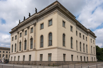 Fototapeta premium A monumental neoclassical building rises with arched windows and sculpted figures along the roof. Cream stone walls form a stately Berlin streetscape.
