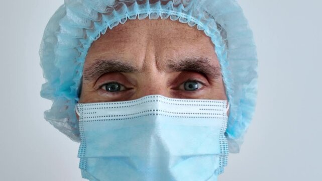 A close-up of a doctor or healthcare worker wearing a surgical mask and cap against a white background looking positively at the camera, indicating that everything will be fine