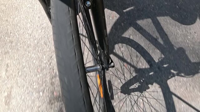 Bicycle fork and wheel close-up with the rider's shadow stretching across a sunlit road, capturing steady forward motion on a countryside ride.