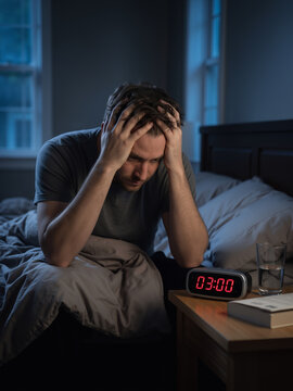 Caucasian man insomnia sufferer sitting on bed in dark bedroom holding head in hands near digital clock showing three am, sleep disorder and mental health awareness vertical banner