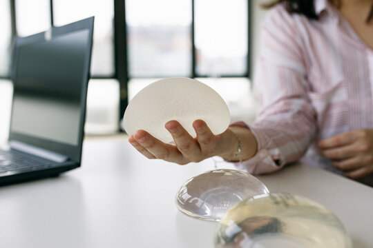 Patient sitting at desk in medical practice holding breast implant
