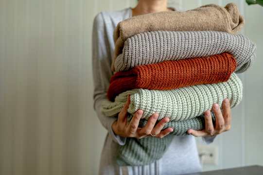 Woman holding multi colored sweaters at home