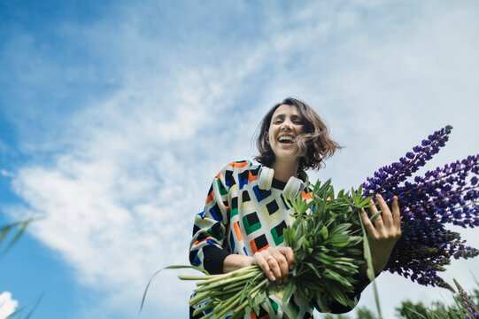 Smiling woman holds a bouquet of lupine flowers in a summer field