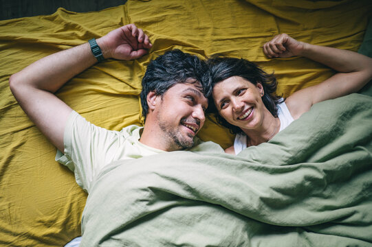 Happy husband and wife lying in bed smiling at each other
