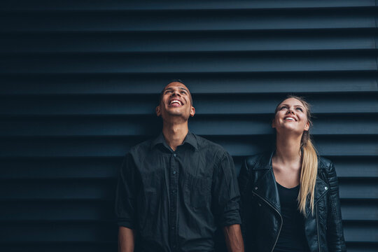 Black dressed young couple standing in front of black facade looking up