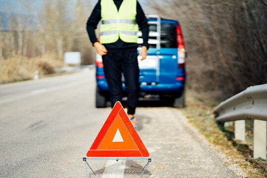 Man putting warning triangle on country road by van breakdown