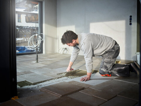 Young tiler applying adhesive on floor at construction site