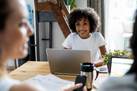 Three women with laptop and documents talking at table