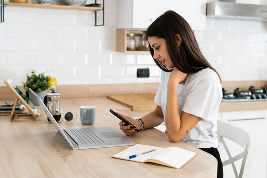 Young woman using cell phone and laptop at home