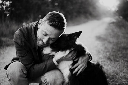 A man hugs his border collie dog outdoors on a nature path