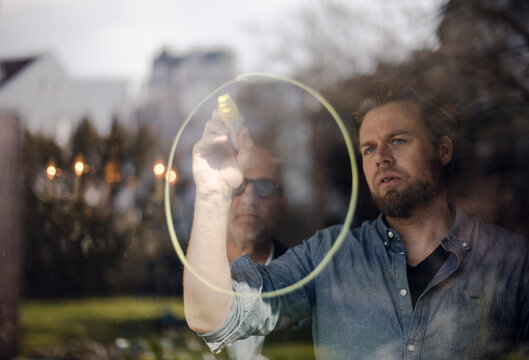 Mature man drawing a circle on window pane, senior man watching