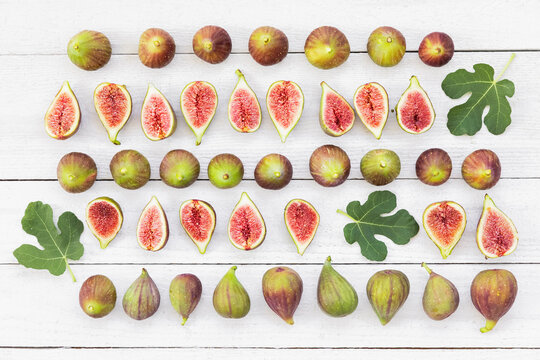 A white wooden table displays fresh whole and cut figs in rows