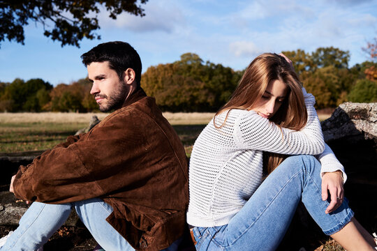 Serious couple sitting back to back in a park