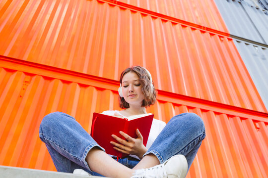 Teenage girl wearing wireless headphones writing in red notebook
