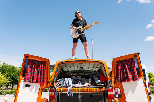 Young woman playing guitar, standing on open van