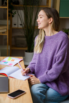 Smiling woman writing in notebook at desk with natural light