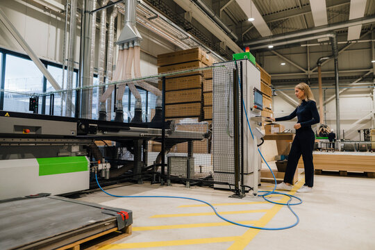Businesswoman operating machine in carpentry factory