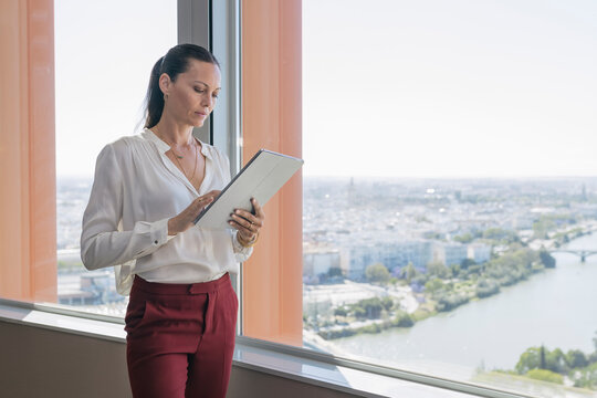 Female professional using digital tablet while standing by window in office