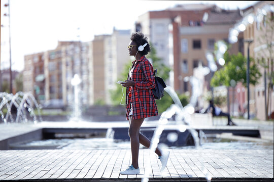 Young woman with backpack, smartphone and headphones walking in the city