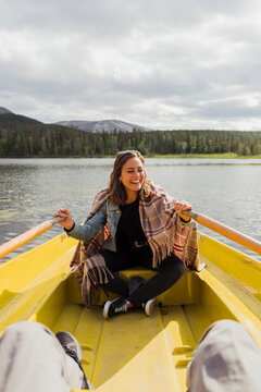 Finland, Lapland, laughing woman wearing a blanket in a rowing boat on a lake