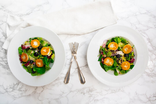 Two plates feature green salad with goat cheese on a marble table