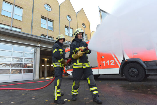 Two firefighters standing on yard exercising with extinguishing water