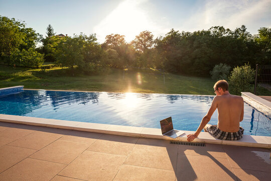 Freelancer sitting with laptop on poolside