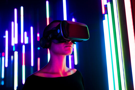 Woman wearing virtual reality simulator near colorful illuminated lights