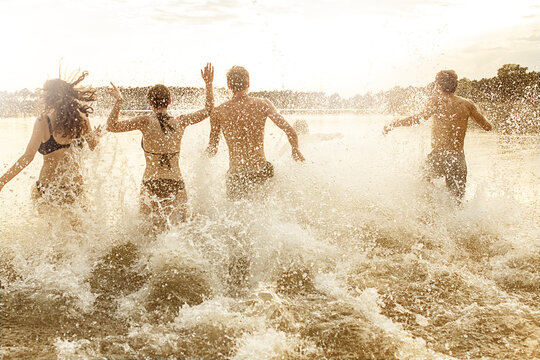 Teenagers run into the splashing water of a lake in summer