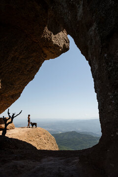 Woman and dog stand on a mountain ledge looking at the landscape