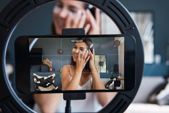 Young woman recording skin care tutorial on smart phone at home