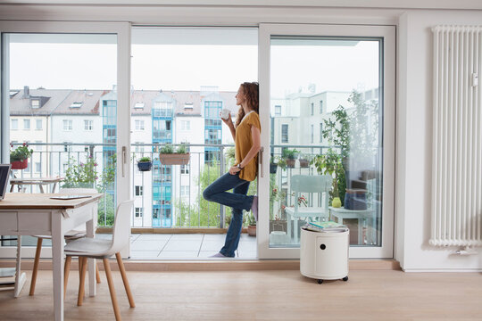 Woman with cup of coffee leaning against balcony door