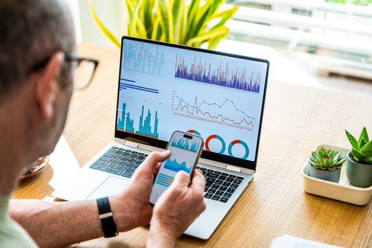 A businessman analyzes financial data on his laptop and smartphone