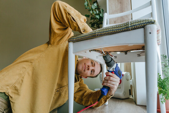Smiling man using drill on chair at home